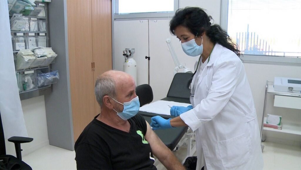 Profesional de la salud administrando una vacuna en el brazo de un adulto con insumos médicos estériles en una clínica moderna
