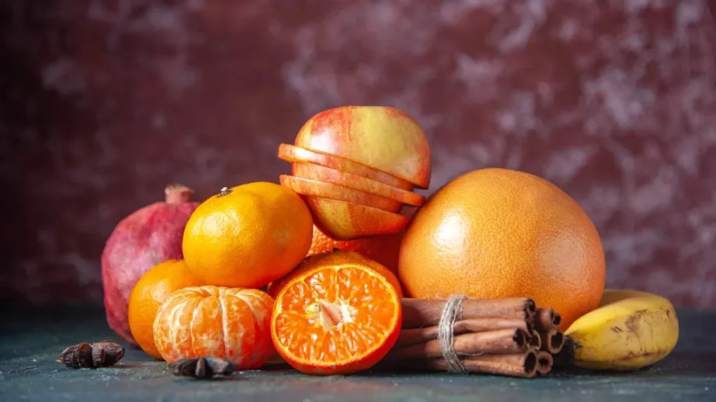 Variedad de frutas frescas de temporada como naranjas, granadas y kiwis sobre una mesa de madera, ideales para fortalecer el sistema inmune en octubre.